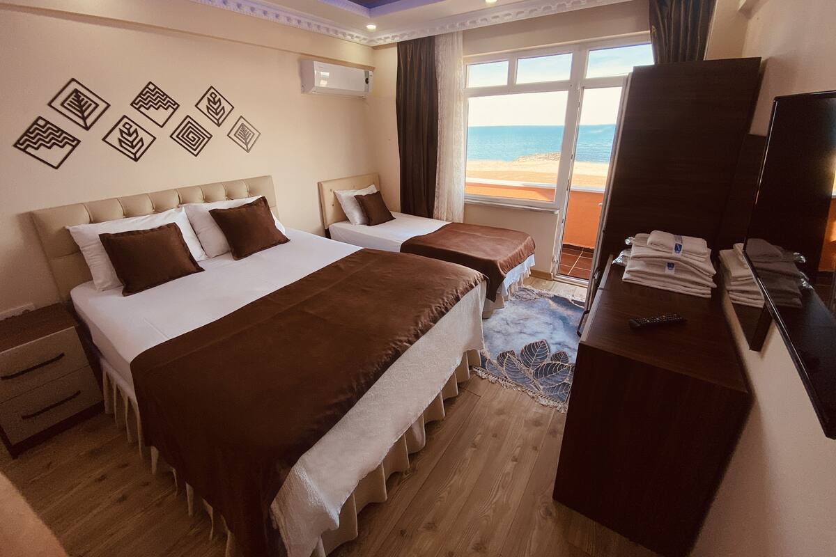 A hotel room with two beds, a desk, a TV, and a view of the beach.