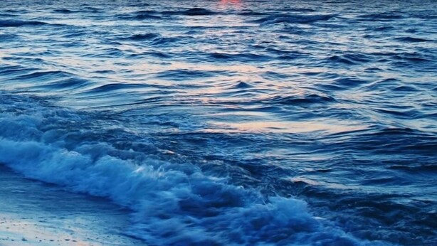 Un coucher de soleil sur l’océan, avec des vagues qui se brisent sur le rivage.
