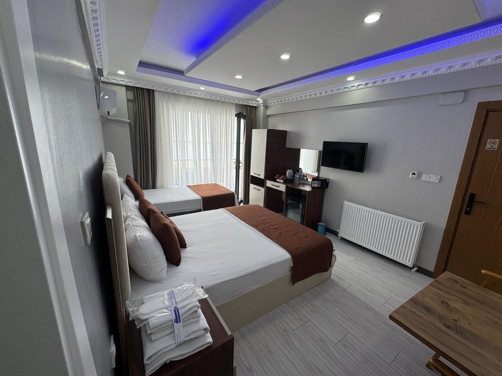 A hotel room with two beds, a desk, a TV, and a radiator.