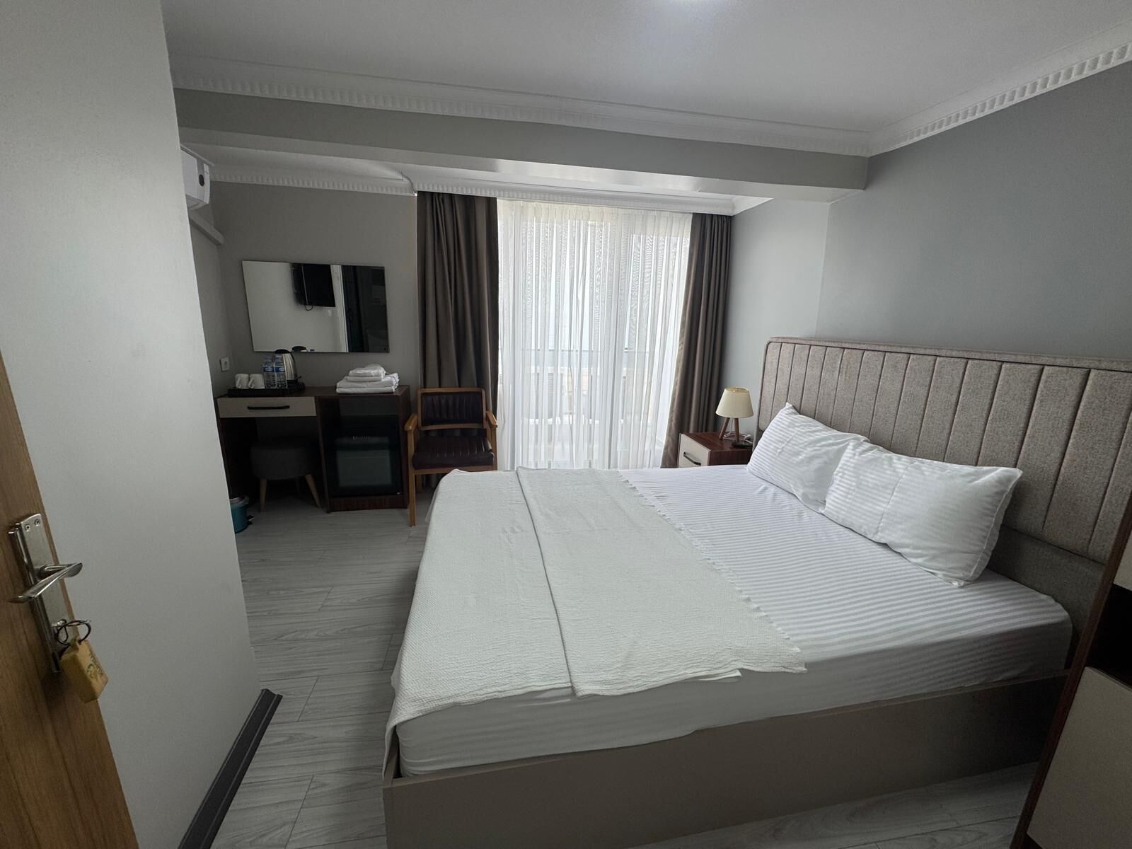 A hotel room with a large bed, a desk, a chair, and a window with curtains.