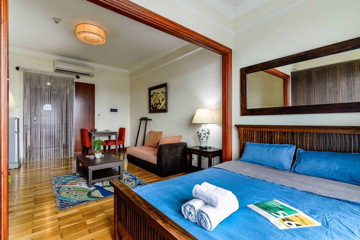 A hotel room with a wooden bed, a desk, a chair, a lamp, and a large mirror.