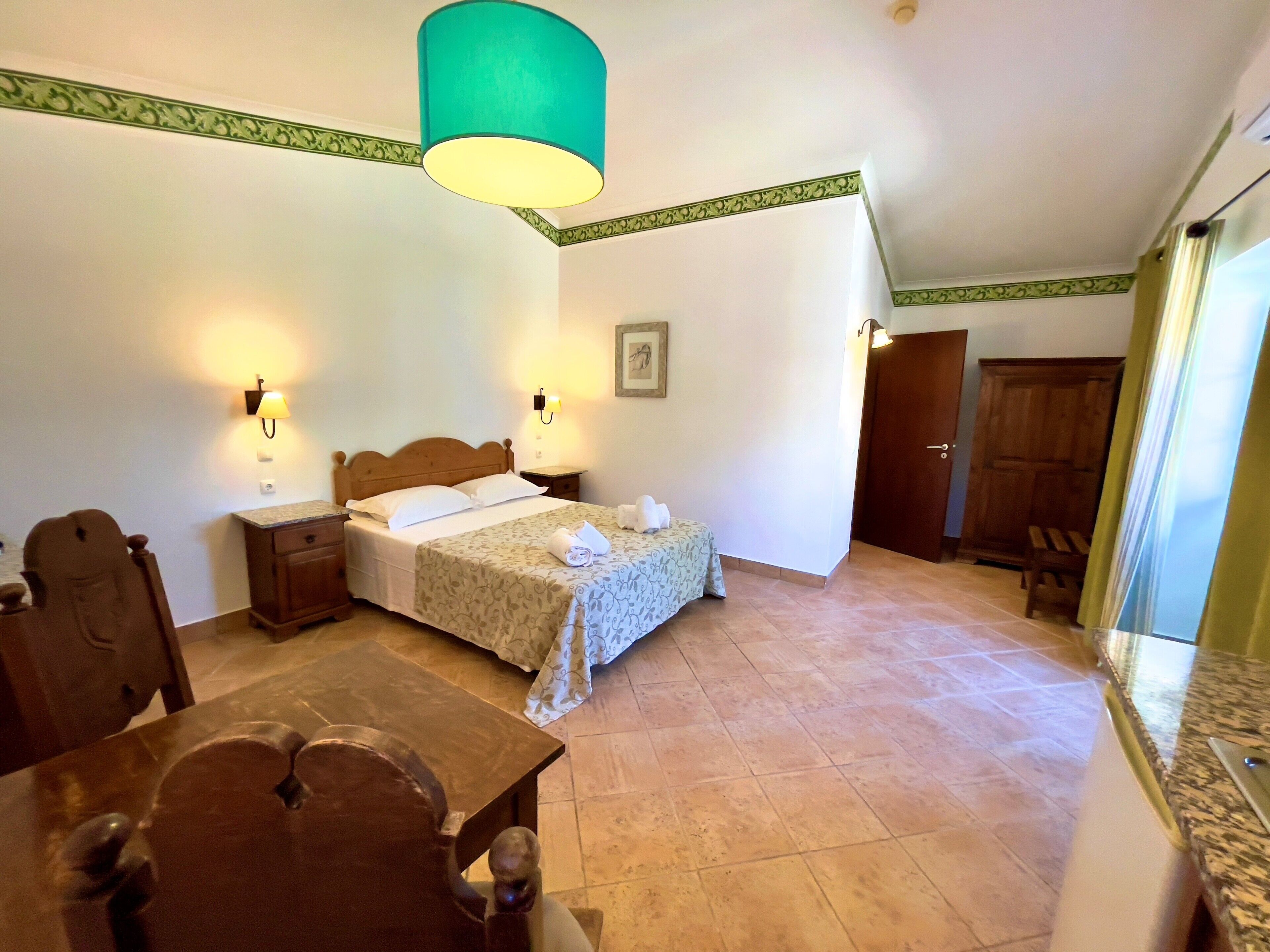 Une chambre à coucher comprenant un lit, des tables de chevet, une chaise en bois, une table à manger et un plafond décoratif de couleur verte.