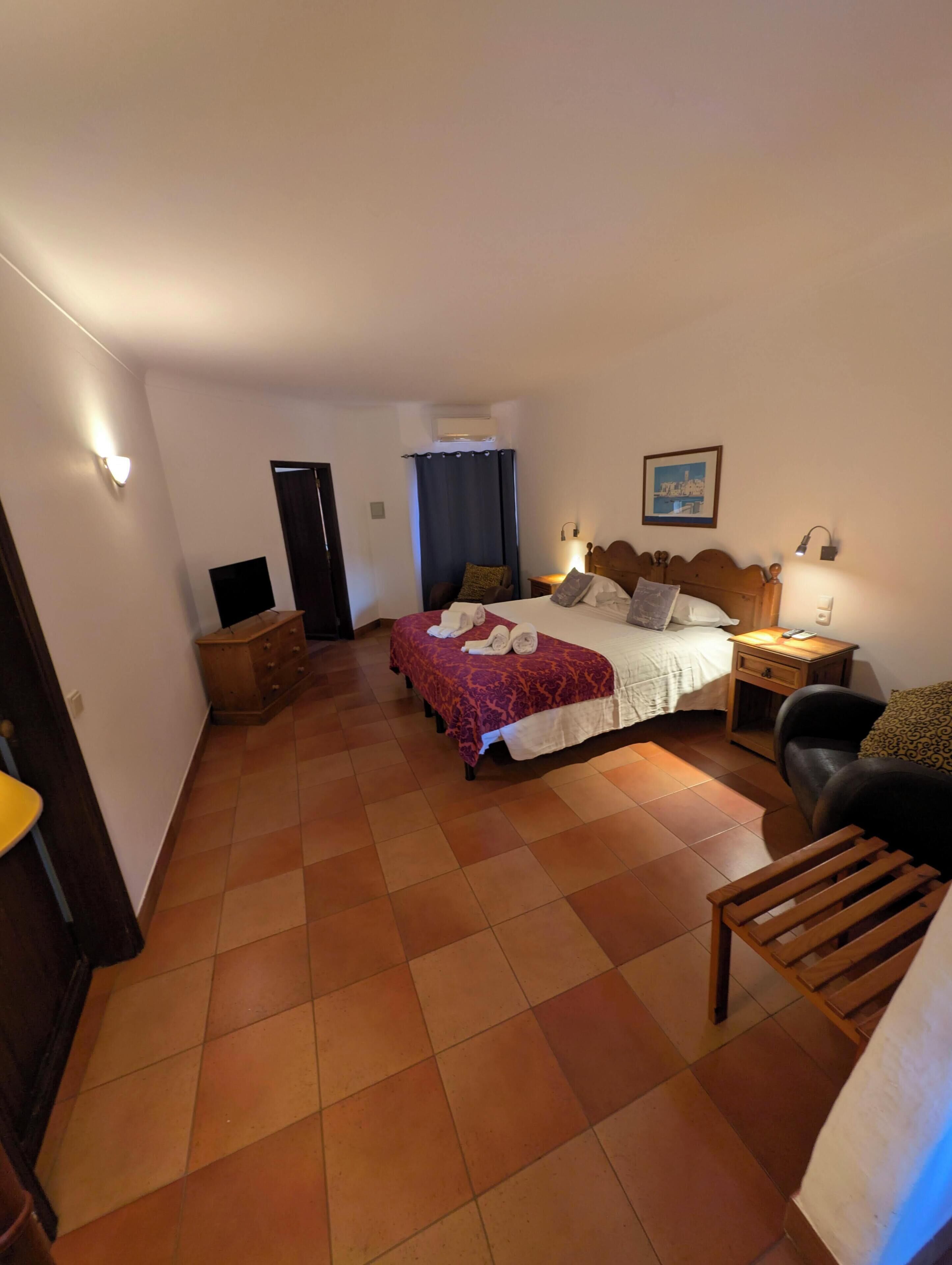 Een slaapkamer met een bed, nachtkastjes, een stoel, een bureau, een kledingkast en een deur.