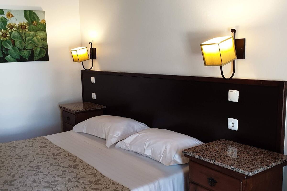 Una habitación de hotel con una cama, dos mesitas de noche y lámparas fijadas a la pared.