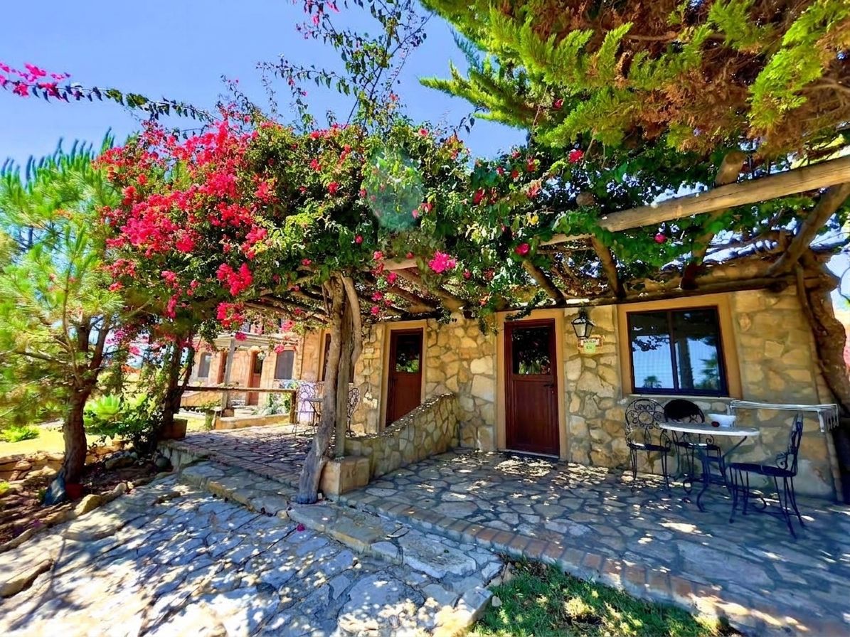 A stone building with a stone staircase, a wooden pergola, and a table with chairs.