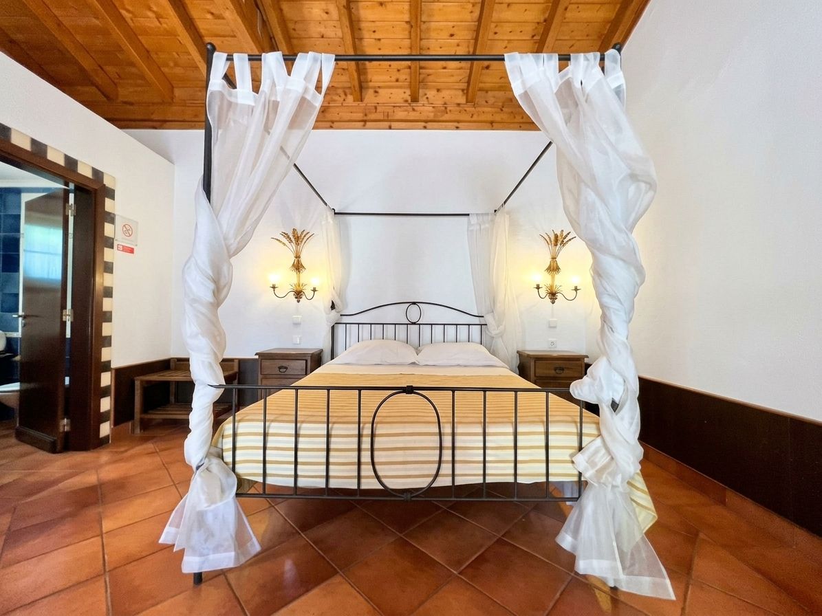A bedroom with a four-poster bed, two bedside lamps, and a wooden ceiling.