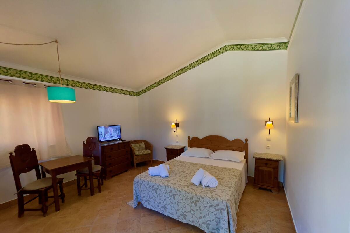 Habitación de hotel con una cama, un escritorio con computadora, dos lámparas de noche y una silla.