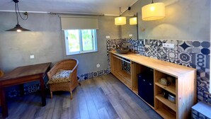 Une cuisine moderne avec un plan de travail en bois, un évier encastré et un crédence décorée. Une fenêtre offre une vue sur la verdure à l’extérieur, et une chaise en osier est placée près de la fenêtre.