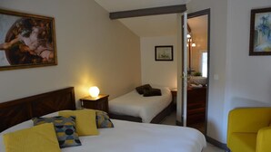 A hotel room with a large bed, two smaller beds, a yellow chair, and a painting on the wall. - Le Mas des Aludes (La Destrousse)