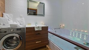 A modern bathroom with a washing machine, a vanity with a mirror, and a large bathtub. - Imperial Apartments Aquarius III (Sopot)