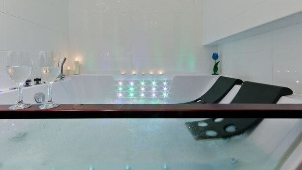 A modern bathroom with a glass-enclosed bathtub, two wine glasses, and a decorative flower. - Imperial Apartments Aquarius III (Sopot)