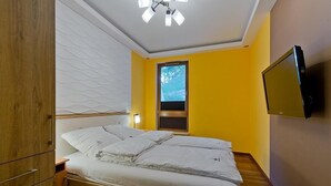 A bedroom with a bed, wooden wardrobe, a television mounted on the wall, and a window with blinds. - Imperial Apartments Aquarius III (Sopot)