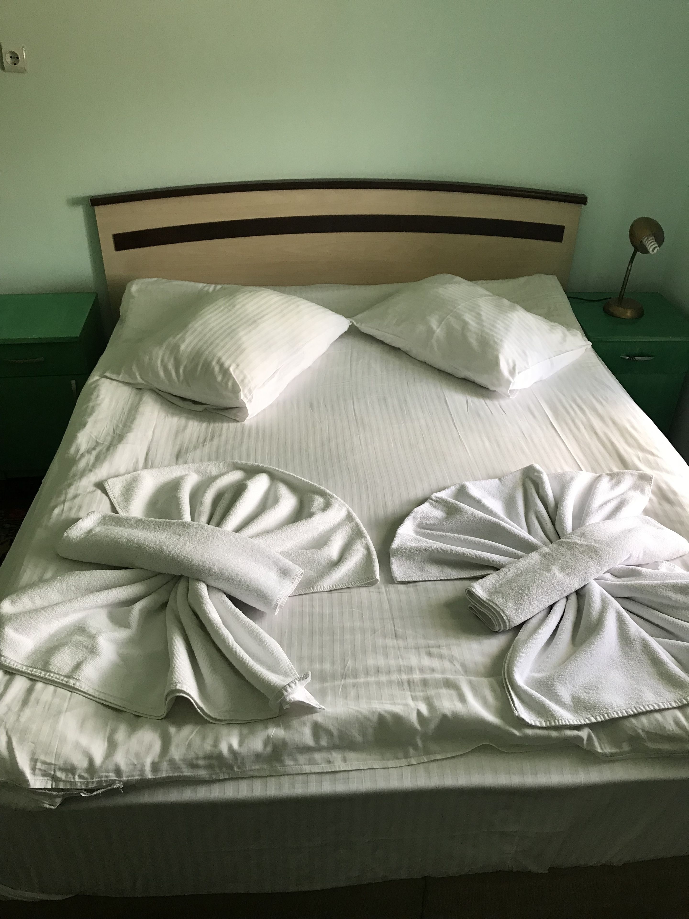 Una cama bien hecha con almohadas y toallas dispuestas en forma de lazo.