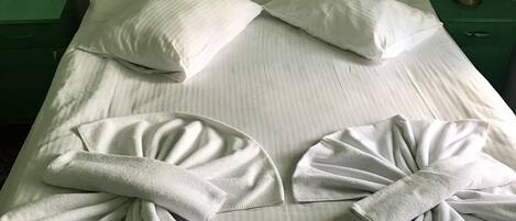 Una cama bien hecha con almohadas y toallas dispuestas en forma de lazo.