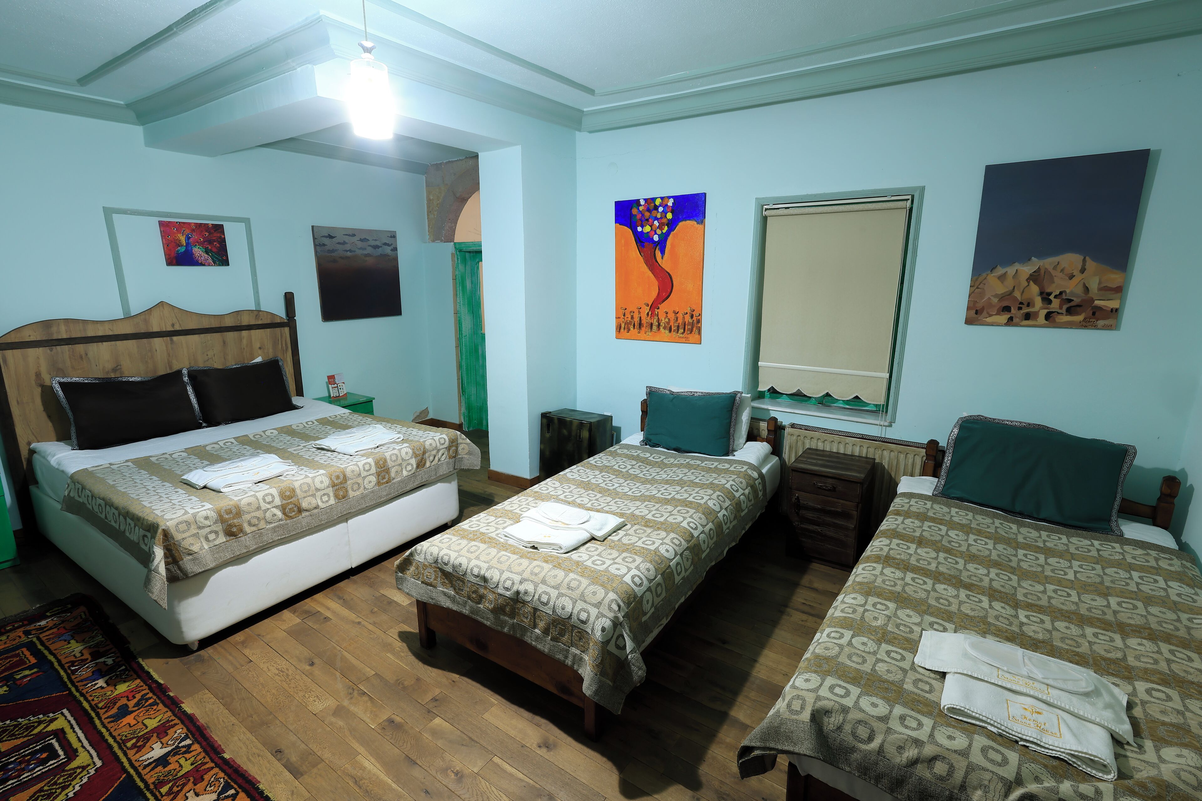 Une chambre d’hôtel avec deux lits, une tête de lit en bois, une fenêtre donnant sur un beau paysage et un tableau accroché au mur.