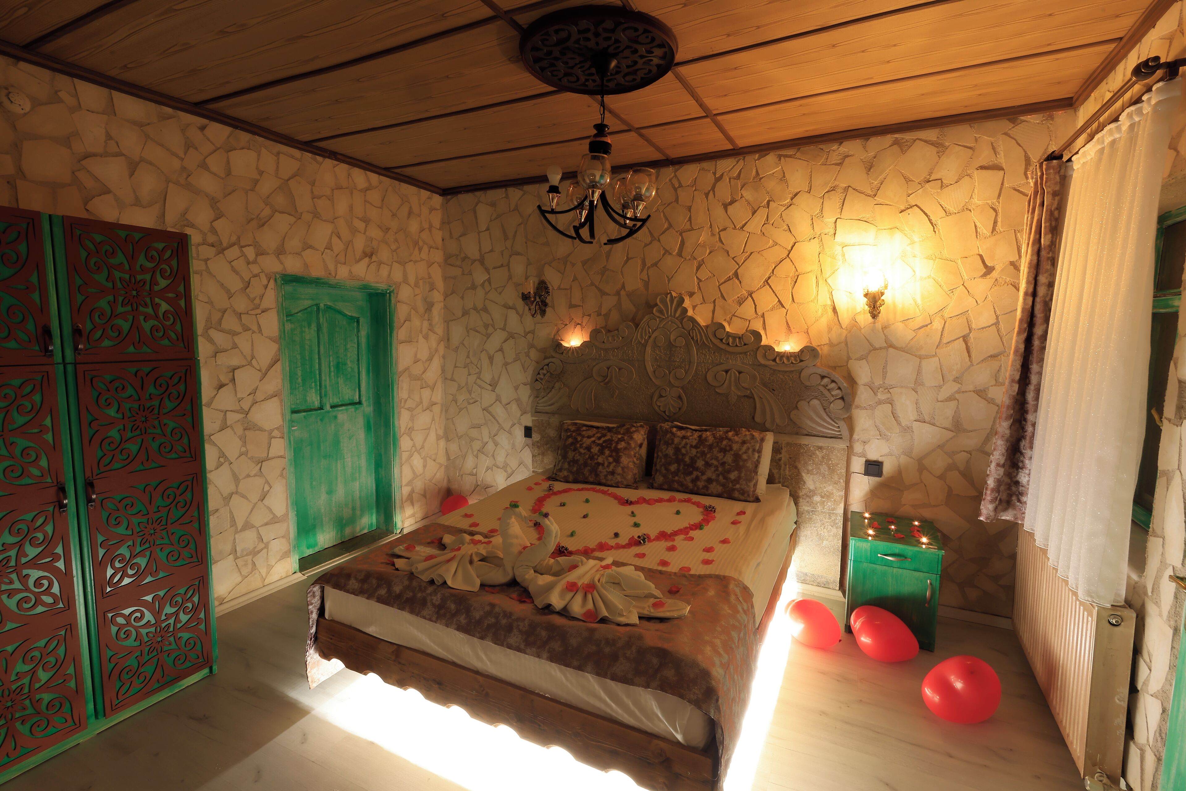 A bedroom with a stone wall, a wooden ceiling, a bed with a heart-shaped decoration, and a green door.