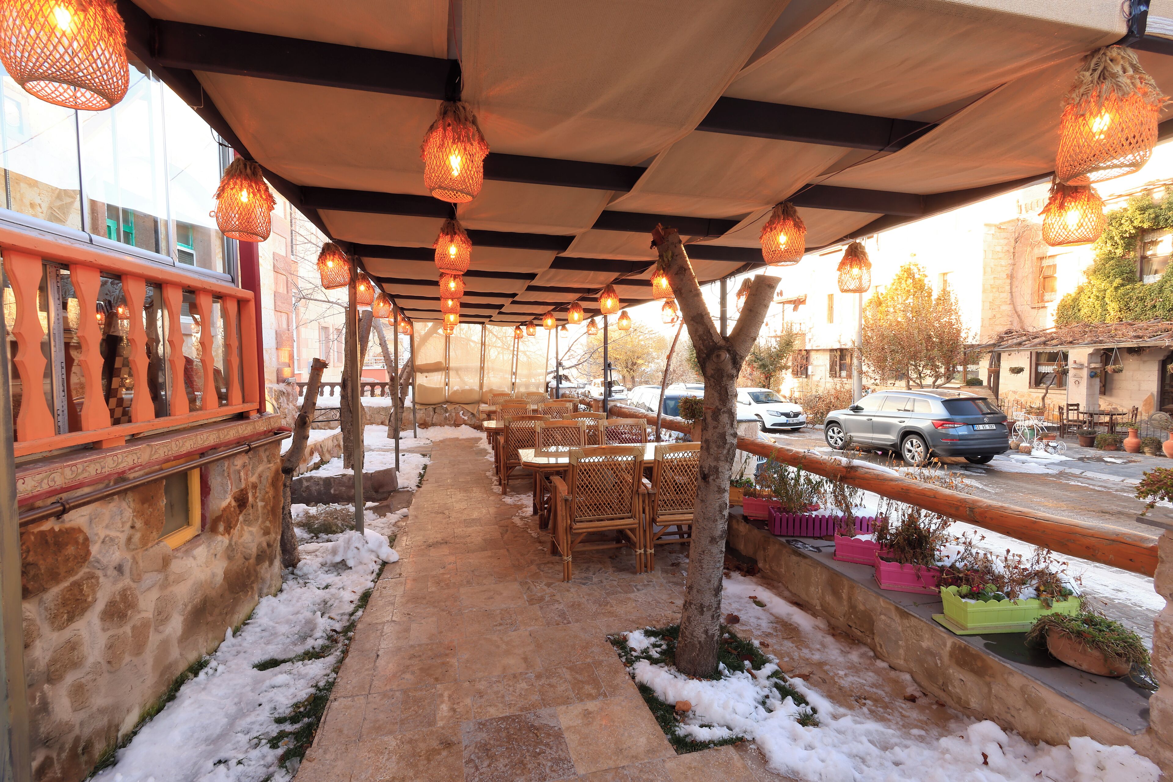 An outdoor seating area with stone walls, wooden tables and chairs, hanging lights, and snow on the ground.