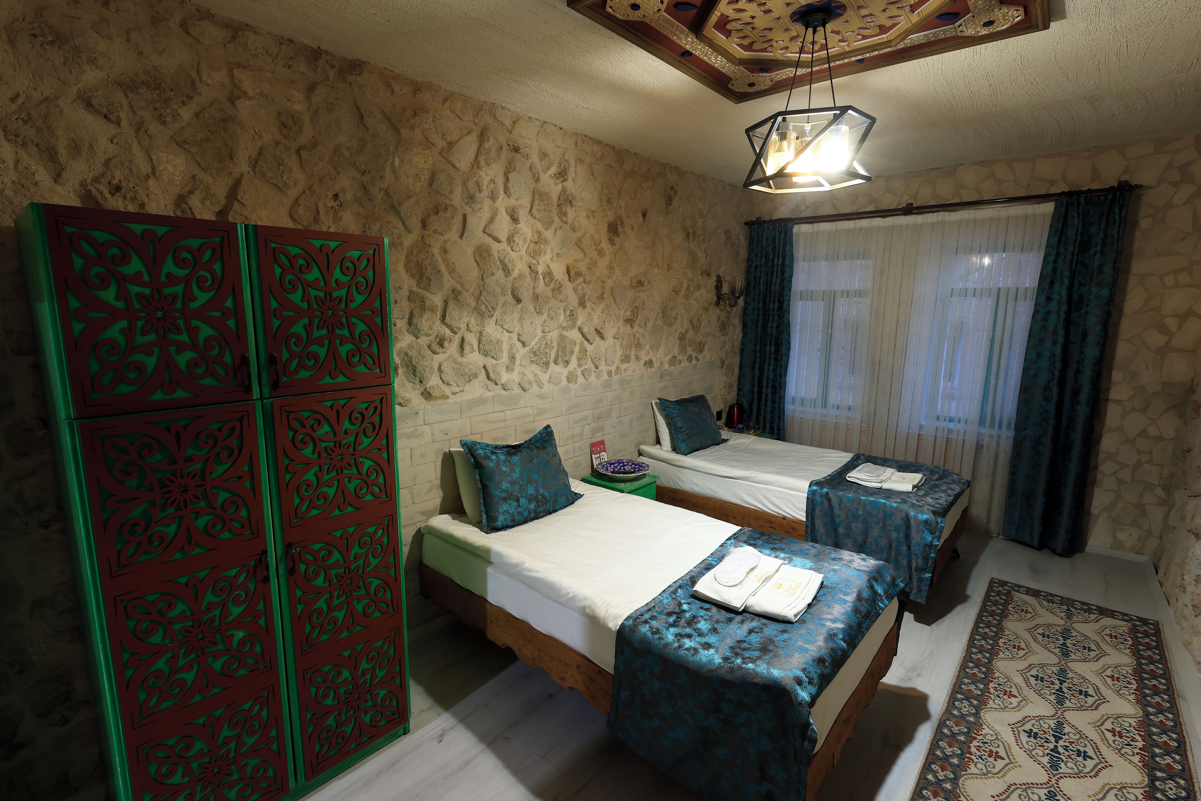 Une chambre avec deux lits, un mur en pierre, un luminaire suspendu et un tapis à motifs.