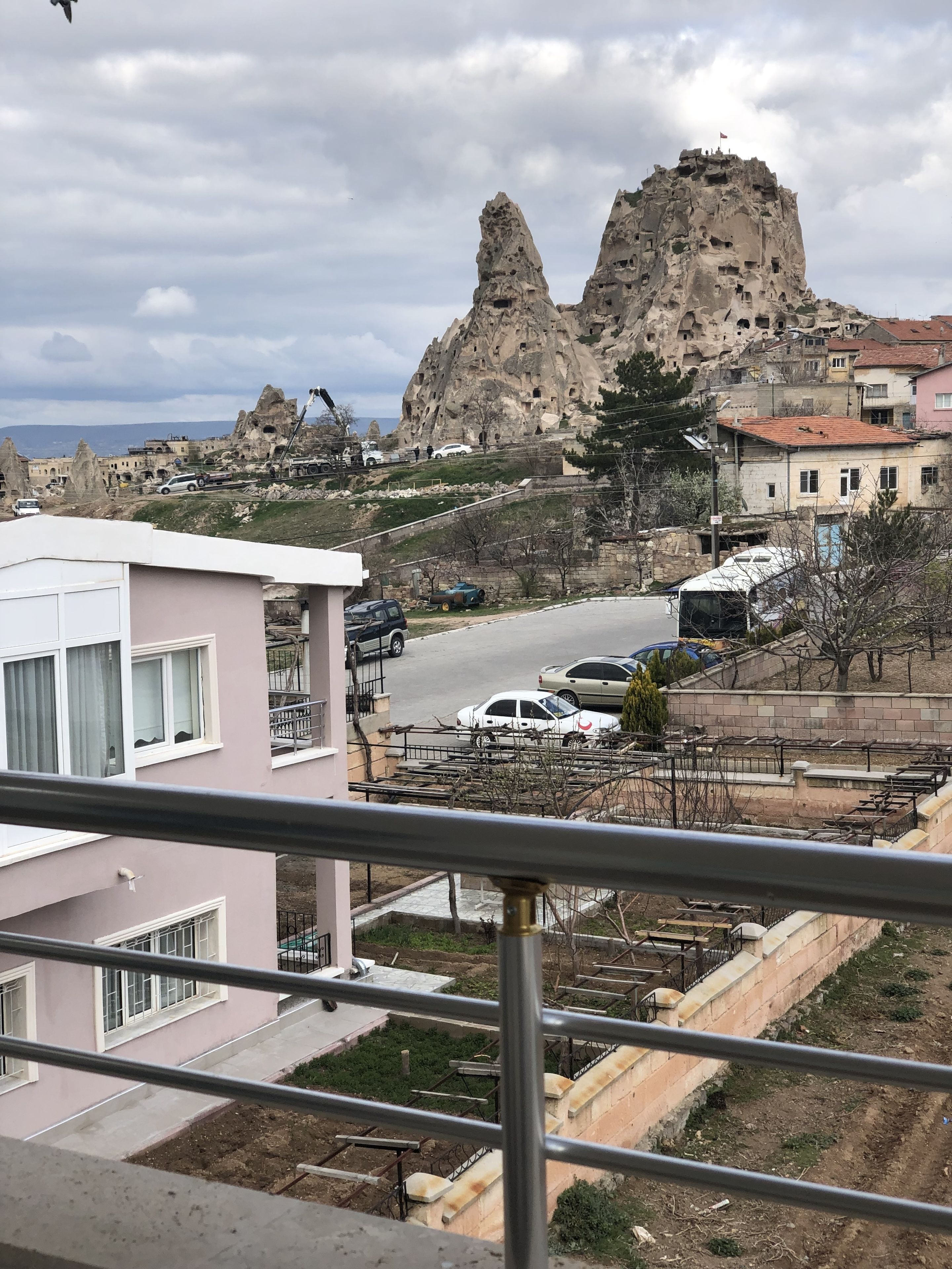 A residential area with a prominent rocky mountain in the background, a road with parked cars, and a pink building in the foreground.