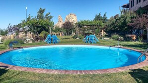 Una piscina con borde de ladrillo, rodeada de césped y árboles.