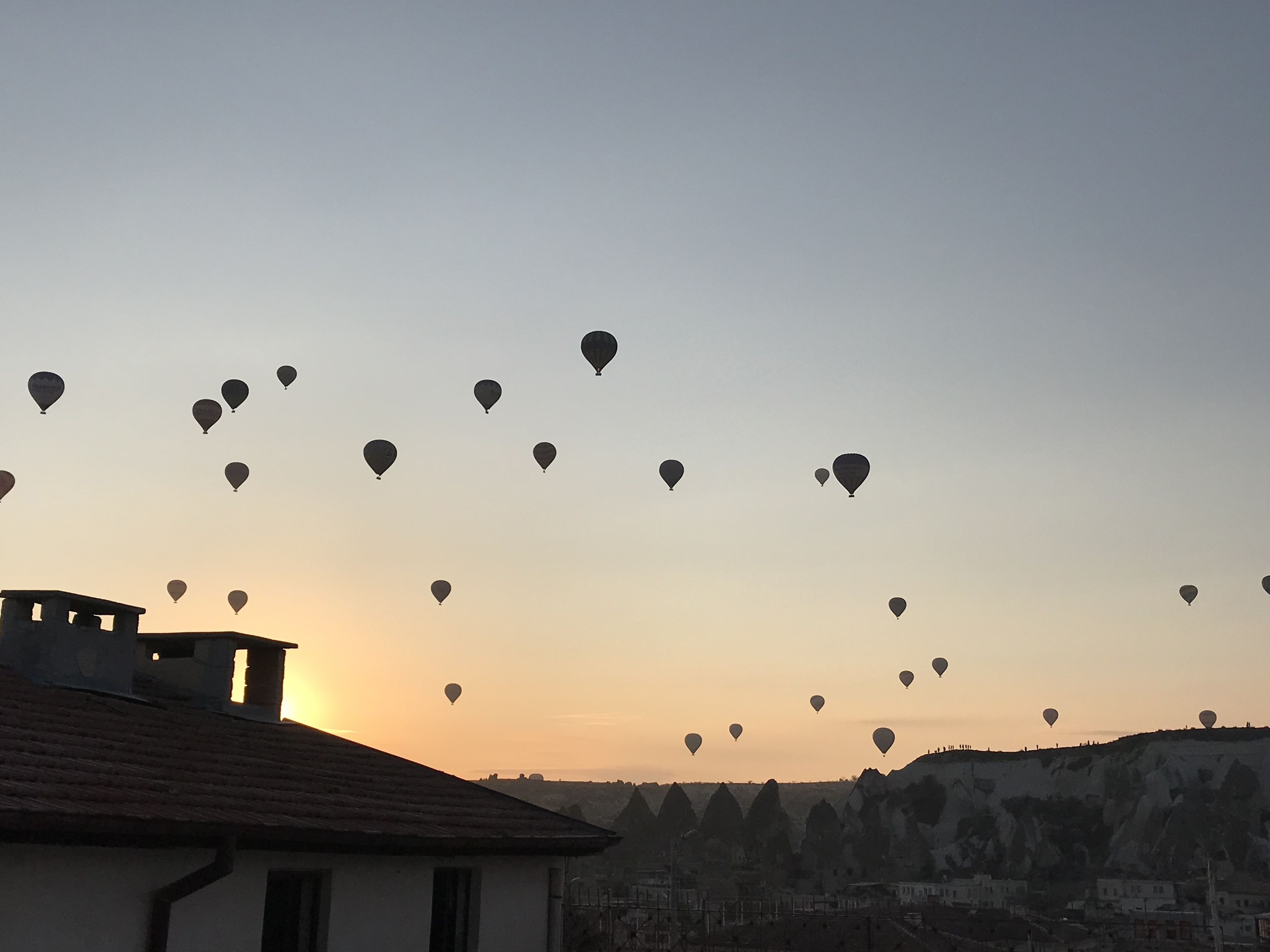 A view of hot air balloons at sunset with a building in the foreground.