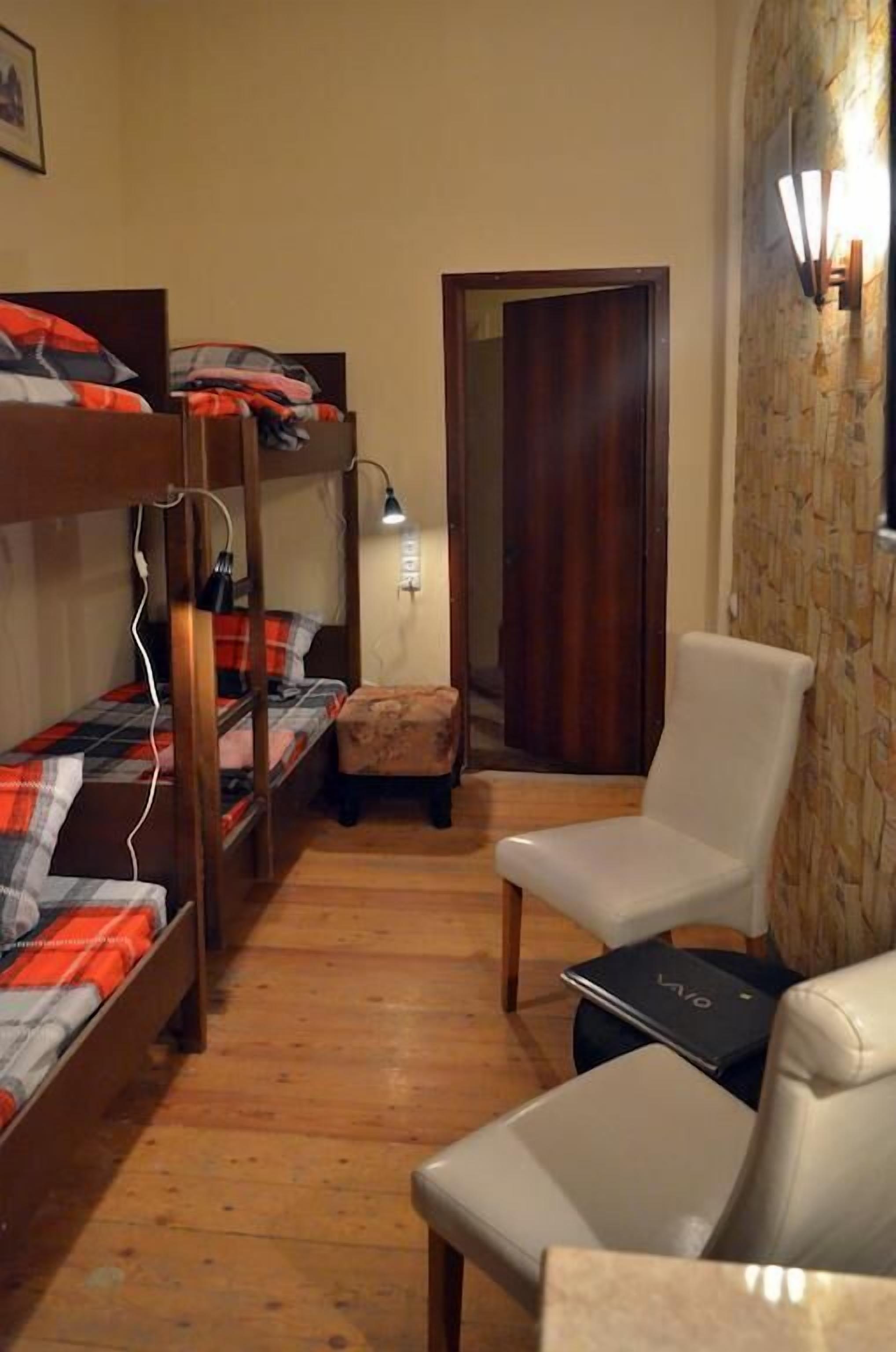 A small room with bunk beds, a chair, a desk with a laptop, and a door leading to another room.