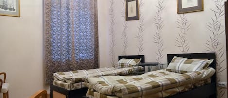 A bedroom with two single beds, a small table, a chair, and patterned wallpaper.