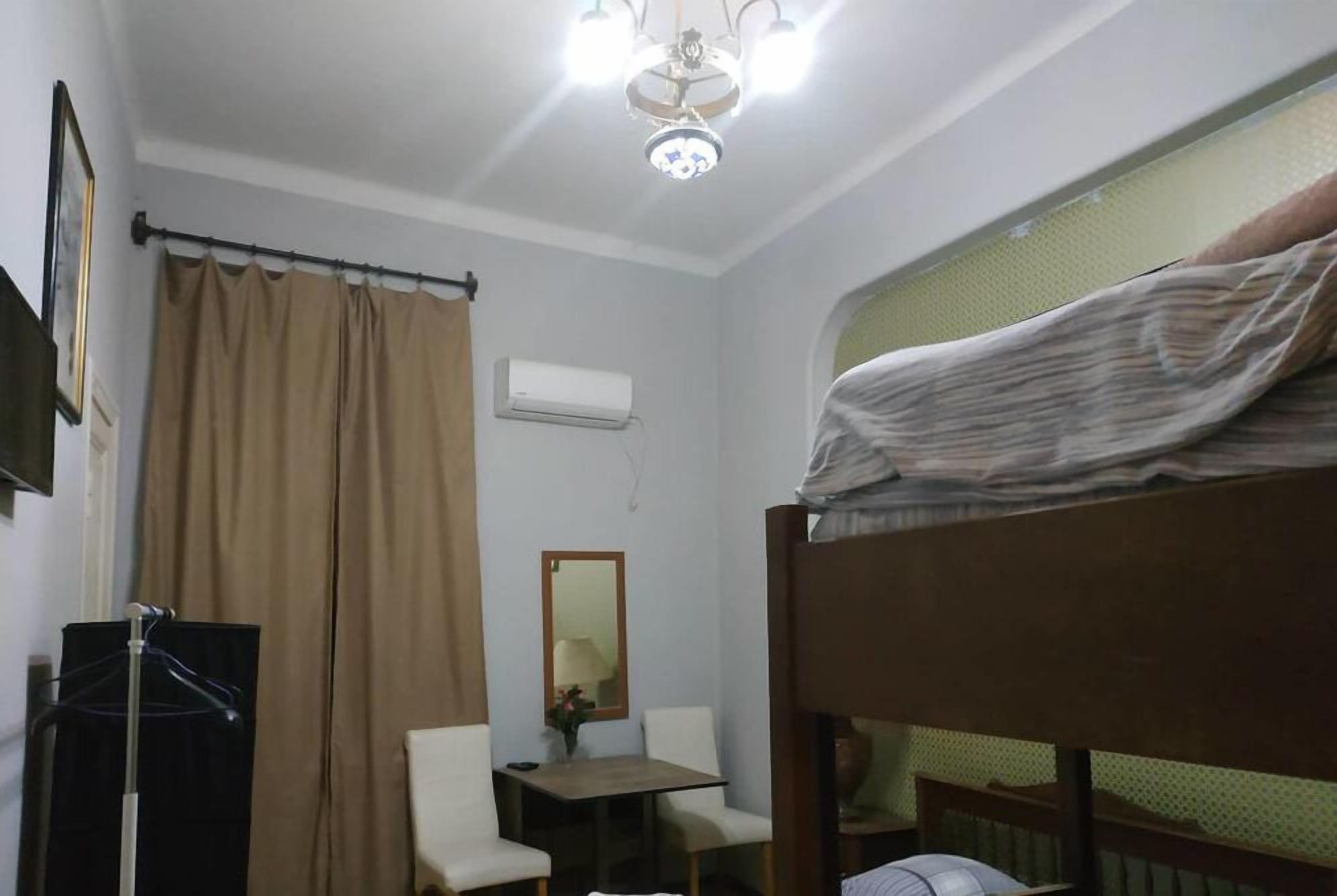 A small, single-room accommodation with a bunk bed, a desk, a chair, a hanging coat rack, a mirror, and an air conditioning unit.