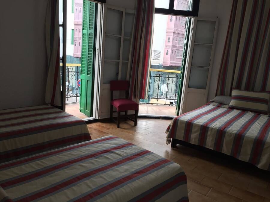 Une chambre avec deux lits, une chaise et un balcon donnant sur des immeubles.