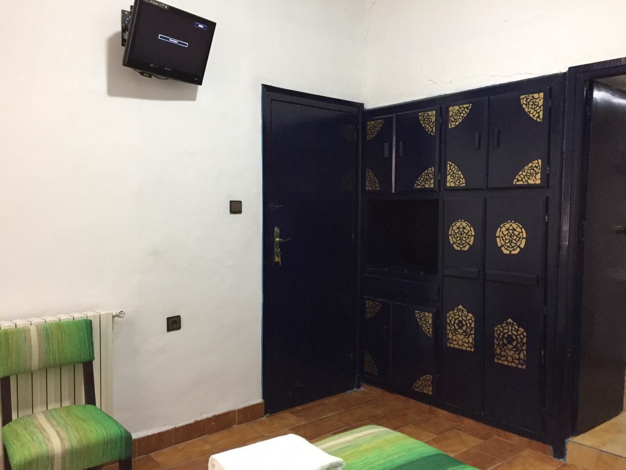Une pièce avec une armoire noire, une chaise verte, une table blanche et un téléviseur fixé au mur.
