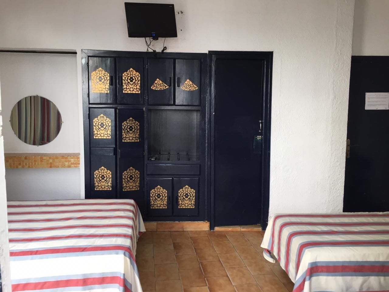 A hotel room with two beds, a TV mounted on the wall, and a wardrobe with decorative panels.