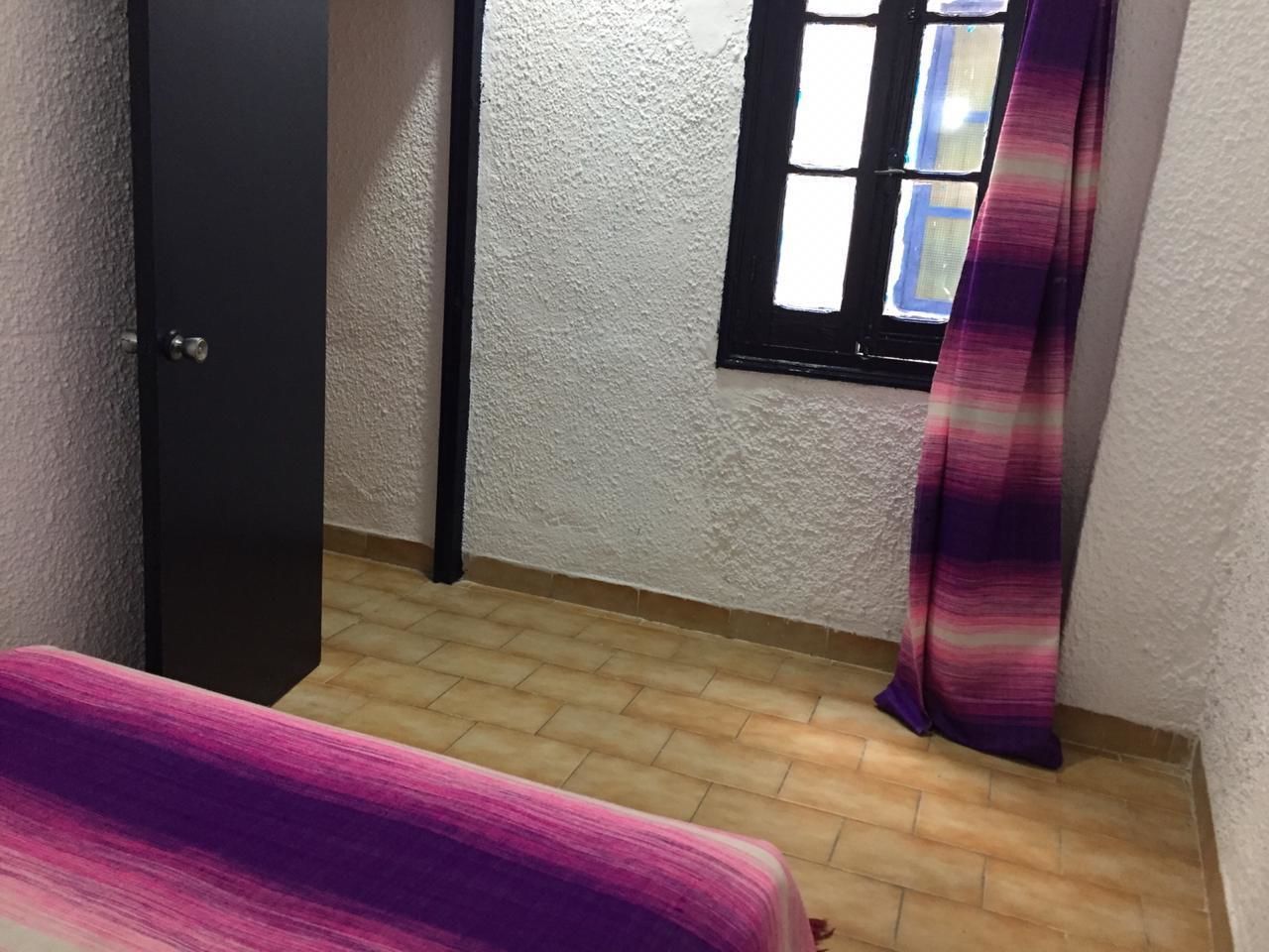 A small room with a bed, a window with a curtain, and a door.