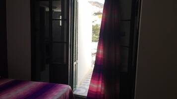 A room with a bed, an open door leading to a balcony, and a view of a mountainous landscape.