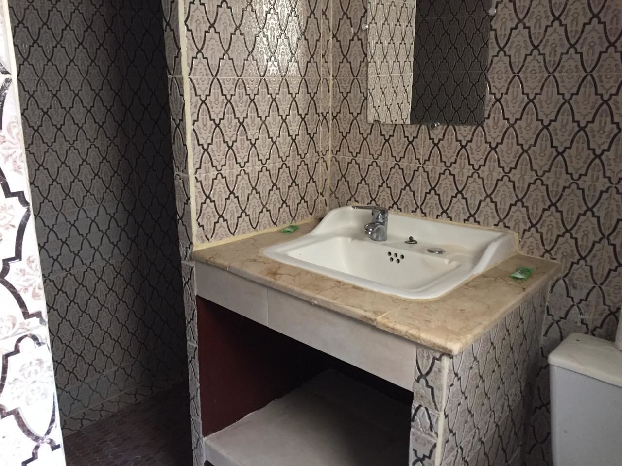 A bathroom with patterned wallpaper, a sink with a marble countertop, and a mirror above the sink.