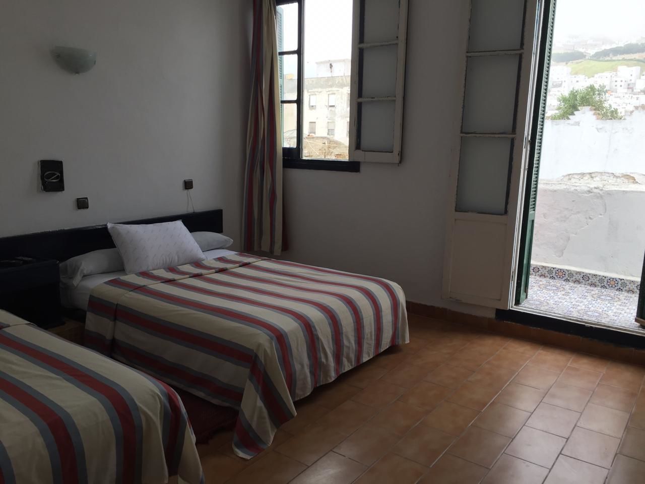 A room with two beds, a window with a view, and a tiled floor.