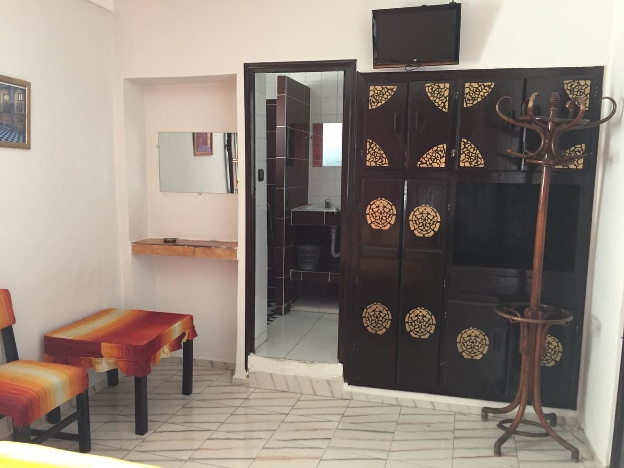 A room with a tiled floor, a wooden cabinet, a mirror, a television, and a coat stand.