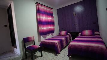 Quarto com duas camas de solteiro, uma cadeira e janela com cortina roxa.