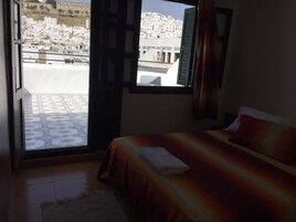 Un dormitorio con cama, ventana con cortinas y vistas a la ciudad.