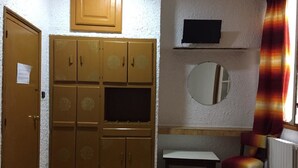 Ett litet rum med en trägarderob, ett skrivbord, en stol, en spegel och en tv som hänger på väggen.