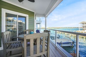 Una terraza de madera con una mesa y sillas, con vistas a un puerto deportivo con barcos y un muelle.