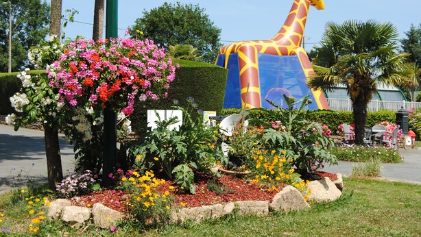Un jardin agrémenté d’une grande sculpture de girafe, de diverses plantes à fleurs et d’un arbuste taillé avec soin.