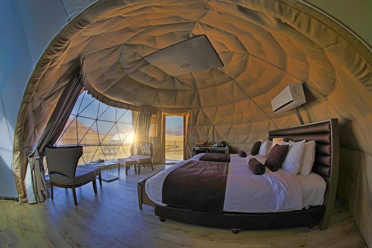 A spacious tent with a large bed, a chair, and a table.