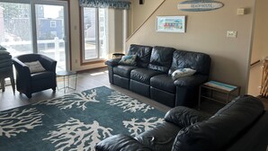 A living room with a black leather sofa, a blue and white patterned rug, and a 'BEACHHOUSE' sign on the wall. - Ocean Views, Watch the breakers from the Deck; B side (Brigantine)