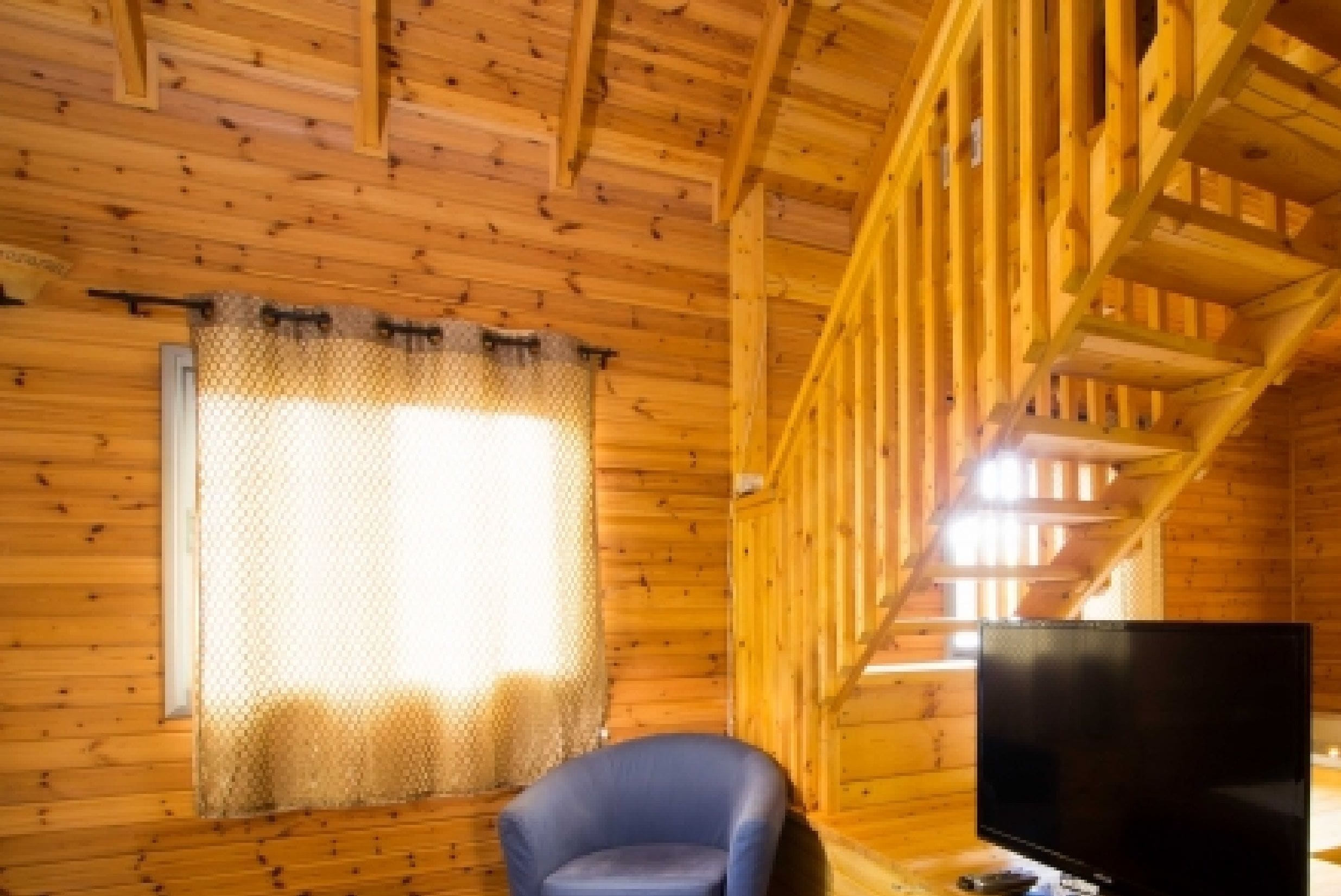 A wooden cabin interior with a television, a chair, and a window with a curtain.
