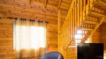 A wooden cabin interior with a television, a chair, and a window with a curtain.