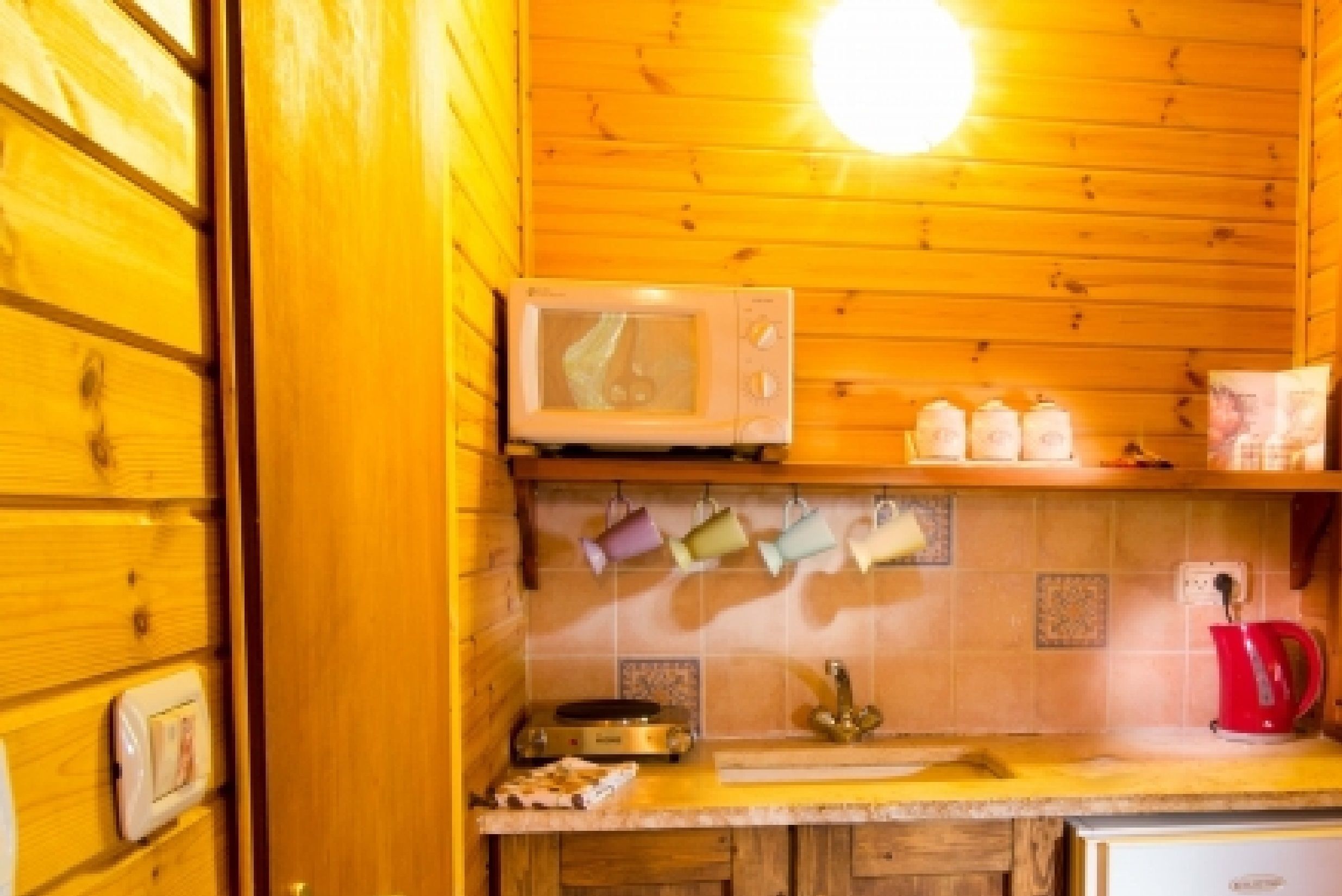 A wooden cabin kitchen with a microwave, a sink, and a red kettle.