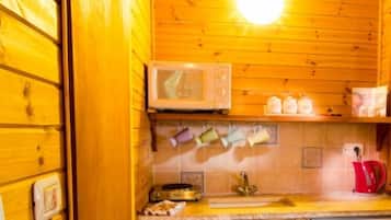 A wooden cabin kitchen with a microwave, a sink, and a red kettle.