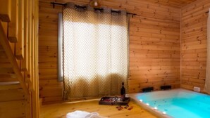 A wooden cabin with a wooden floor, a window with a mesh curtain, a hot tub, and a tray with a bottle and glasses. - Indigolan (Ma'ale Gamla)
