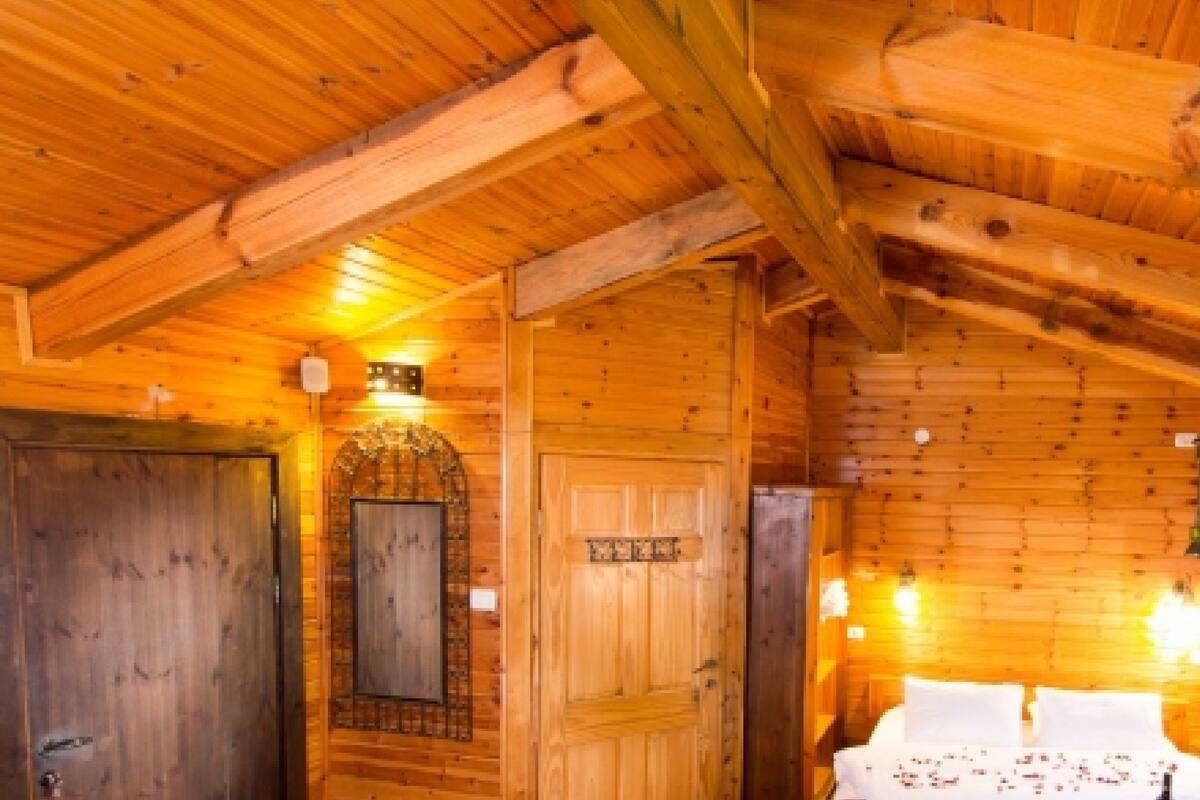 Interior de una cabaña de madera con una cama, una puerta de madera y un espejo.