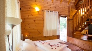 A wooden cabin room with a bed, a nightstand, a wall-mounted lamp, and a staircase. - Indigolan (Ma'ale Gamla)